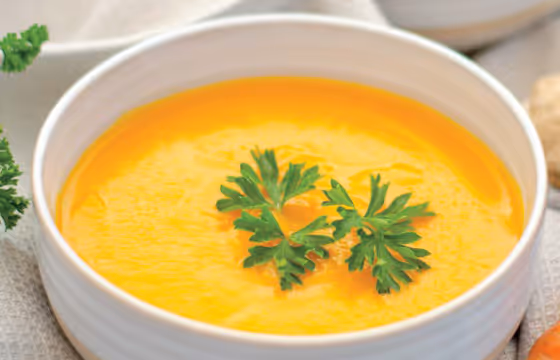 White bowl filled with creamy orange soup garnished with two sprigs of fresh parsley.