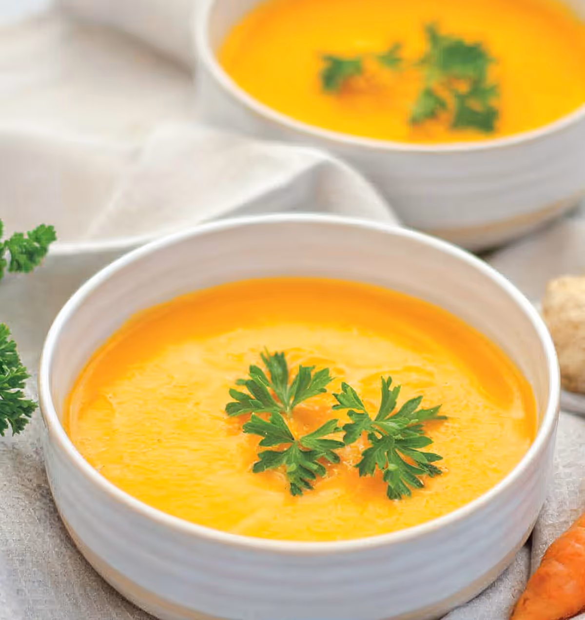 Two bowls of creamy orange soup garnished with fresh parsley on a light cloth background.