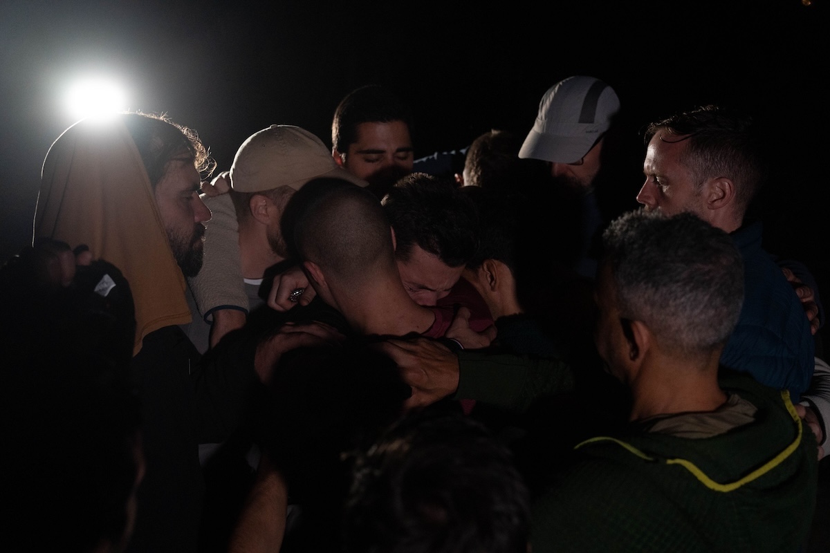 The men embrace in a group huddle at night at The Return of Men retreat, Wim's Land, Comporta, November 2024.