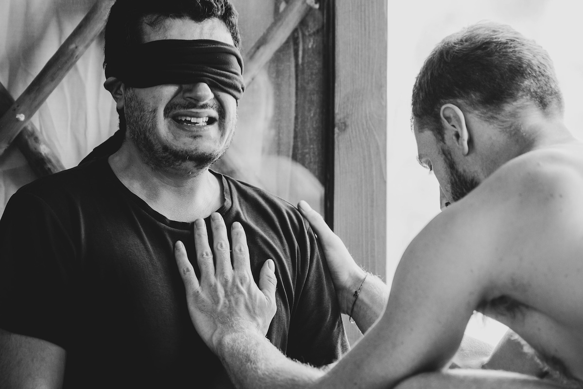 A blindfolded man smiles through tears as a hand rests on his chest at The Return of Men retreat, November 2024.