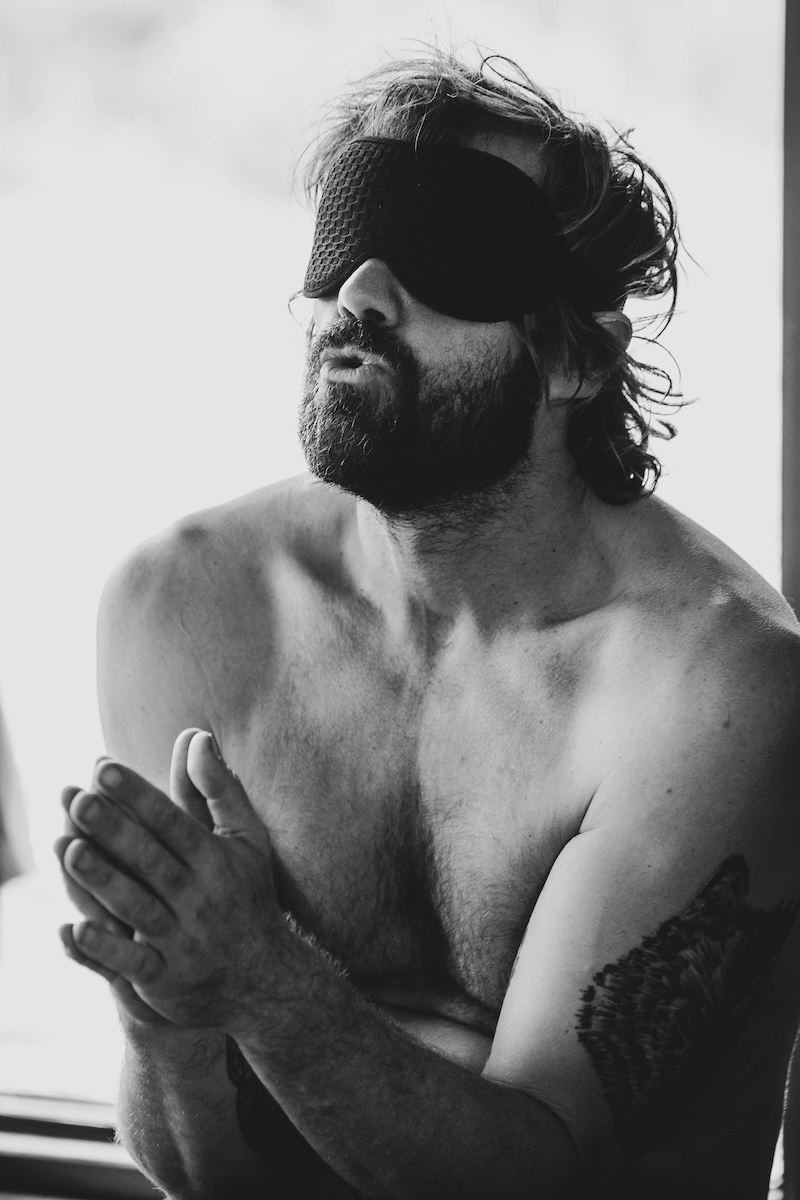 A blindfolded man clasps his hands to his chest during inner work at The Return of Men retreat, Comporta, 2024.