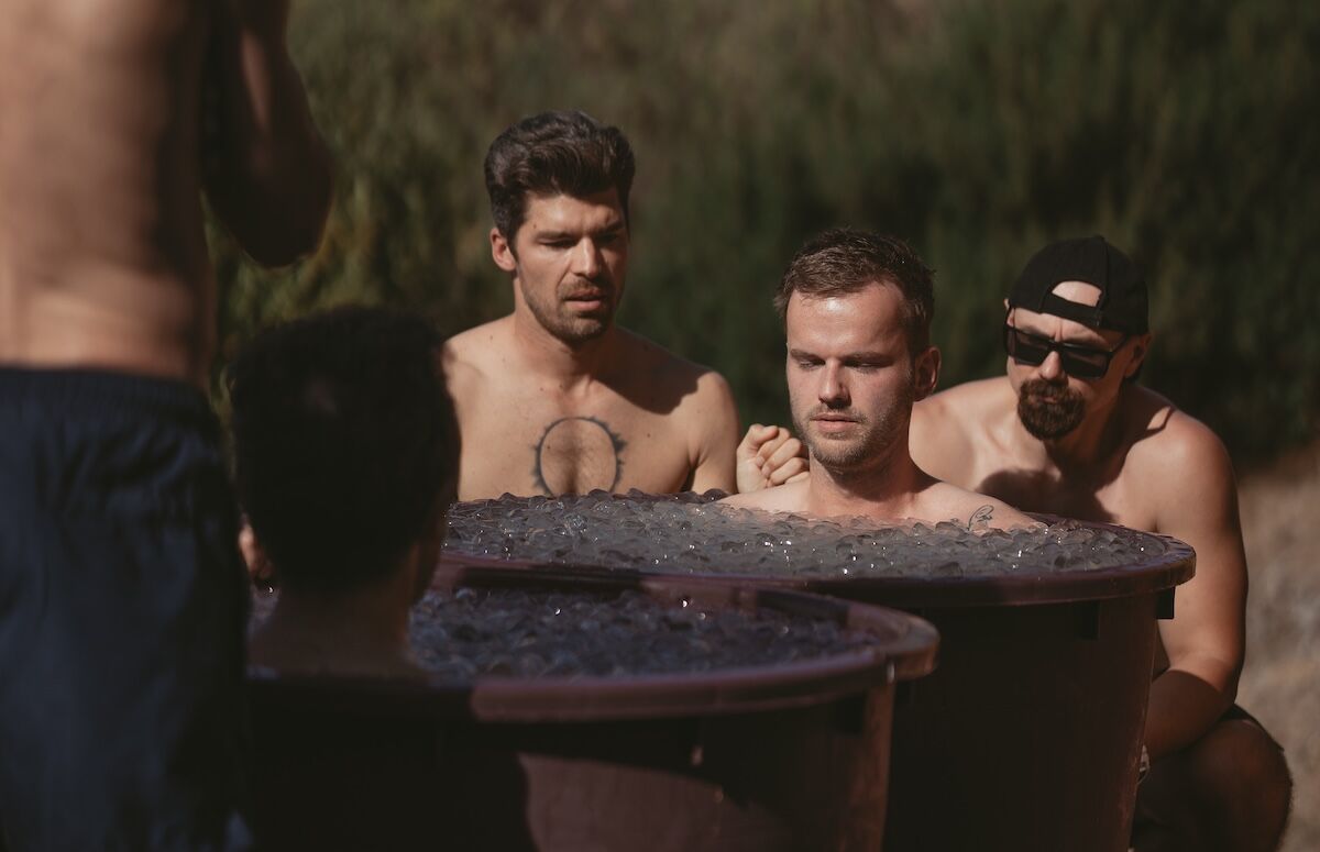 Man sitting calmly in an ice bath supported by others, symbolising lasting inner peace and grounded presence.