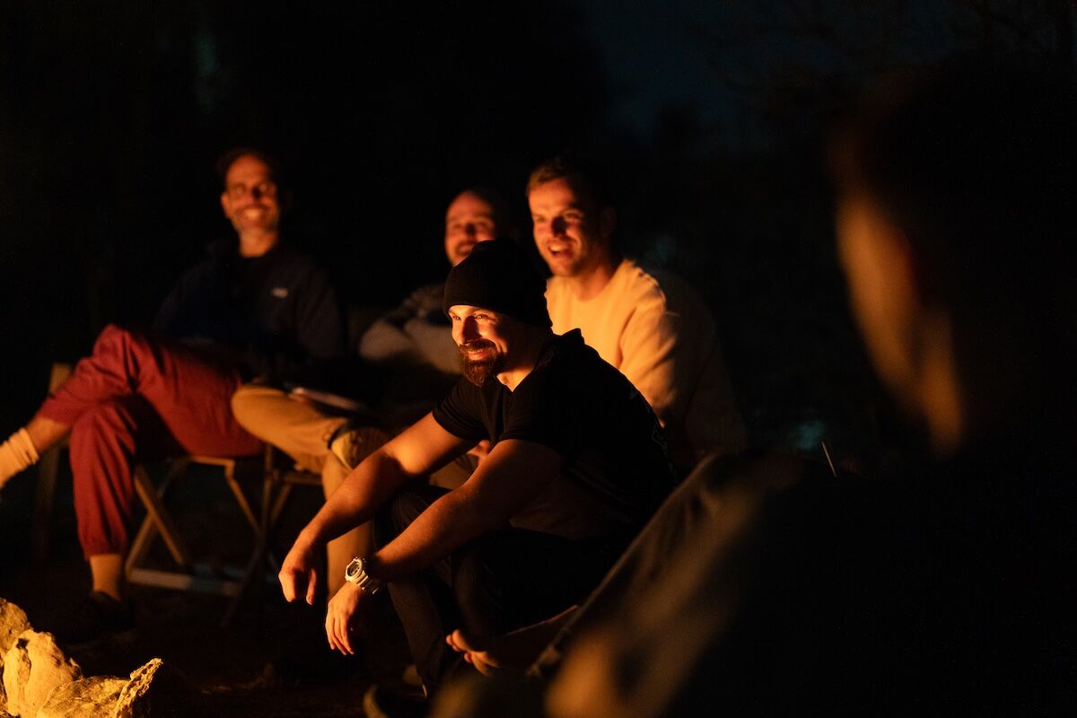 Men laughing together in the firelight at The Return of Men retreat, BioVilla, Portugal, October 2025.