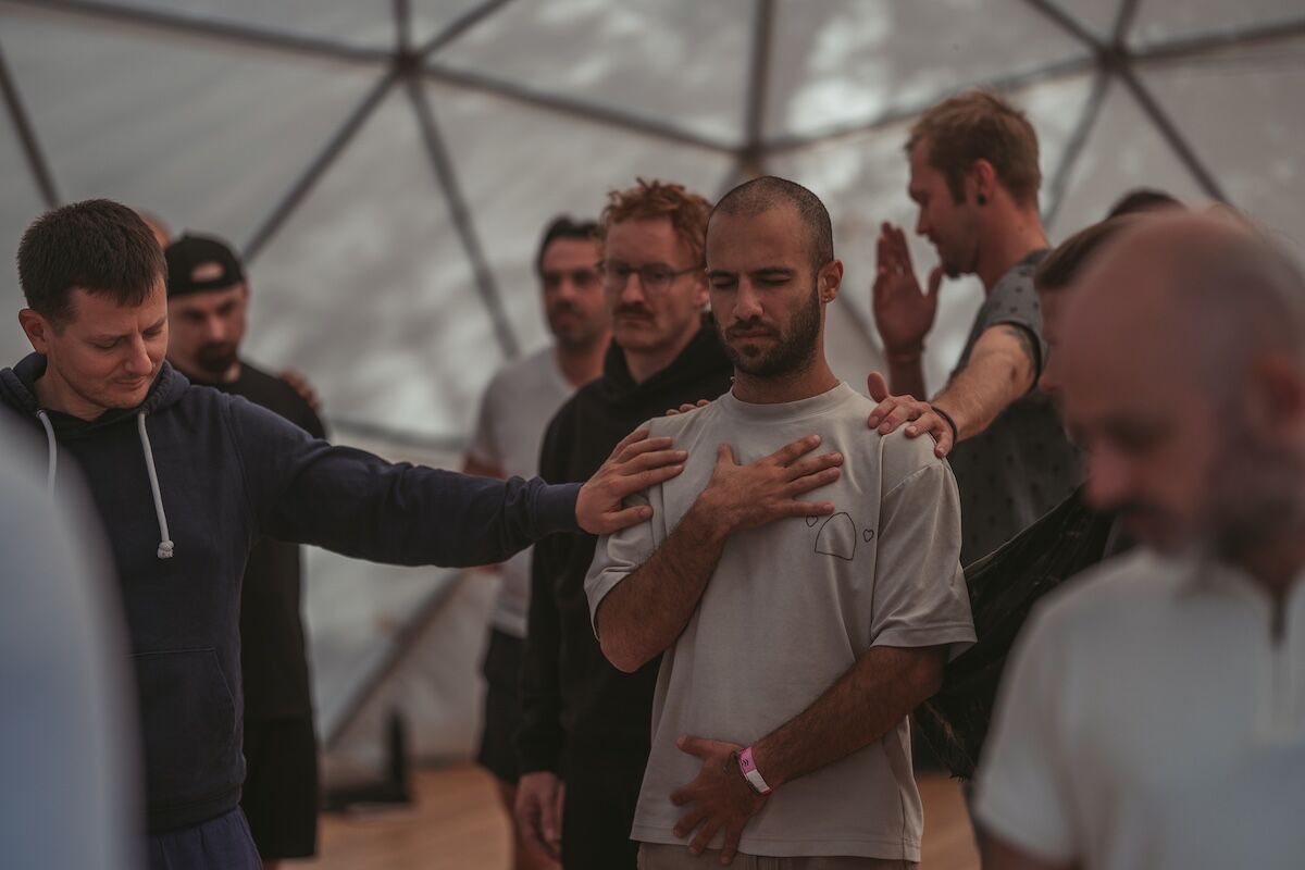 A man with a hand on his chest is held by the hands of others inside the dome at The Return of Men retreat, 2025.