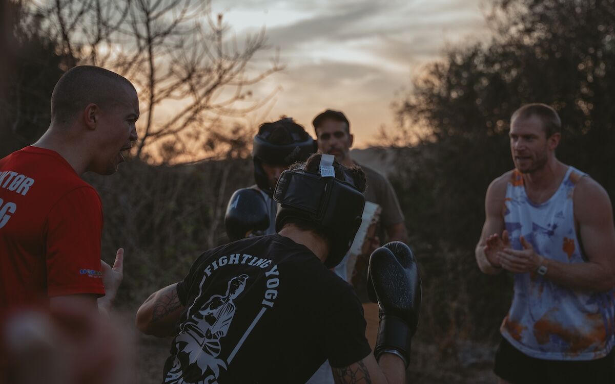 Men in headguards talk between rounds at dusk at The Return of Men retreat, Portugal, 2025.