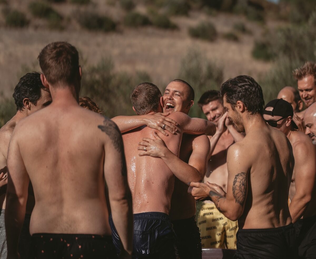 Group of men laughing and hugging, symbolising brotherhood, authenticity, and raw, honest connection without masks.