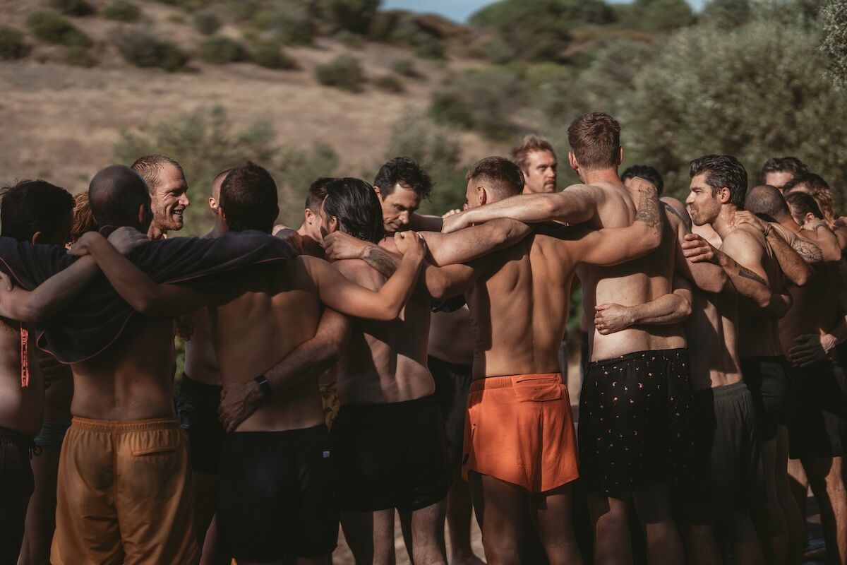 Men standing in a circle embracing and smiling in nature after an ice bath ritual, symbolising brotherhood, presence, and renewed vitality.