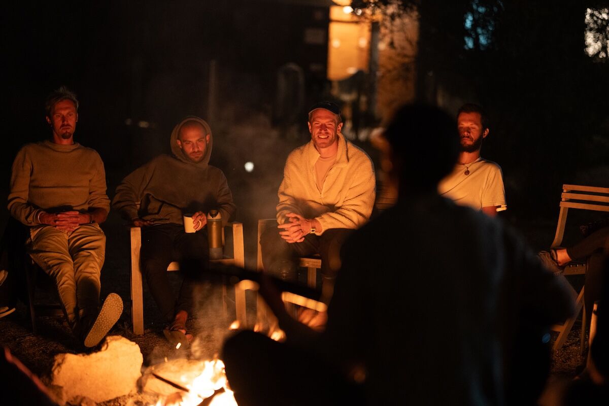 Four men listen by the fire as another speaks at The Return of Men retreat, Arrábida, October 2025.