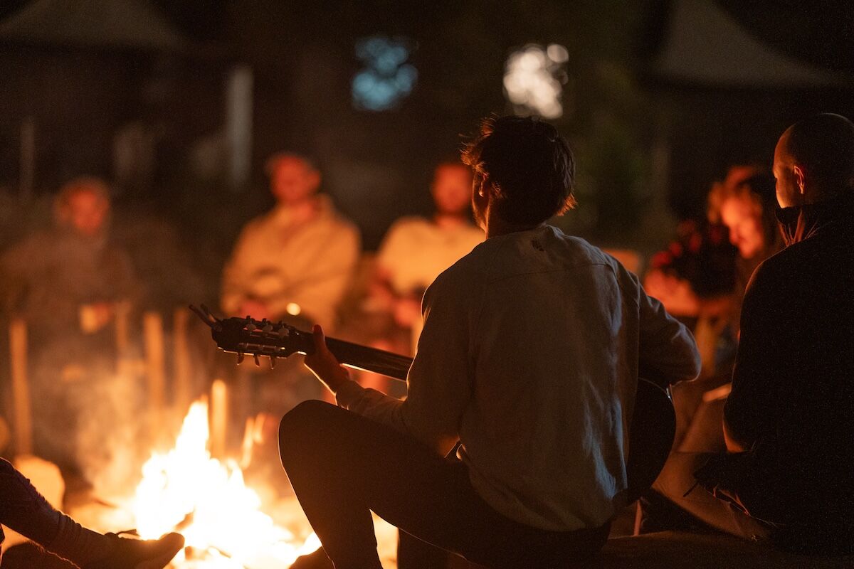 A man plays guitar by the fire as the circle listens at The Return of Men retreat, Portugal, October 2025.