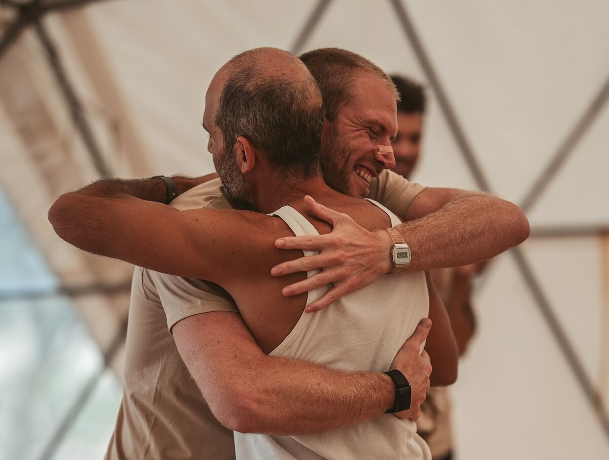 Two men grin through a hard embrace inside the dome at The Return of Men retreat, Portugal, October 2025.