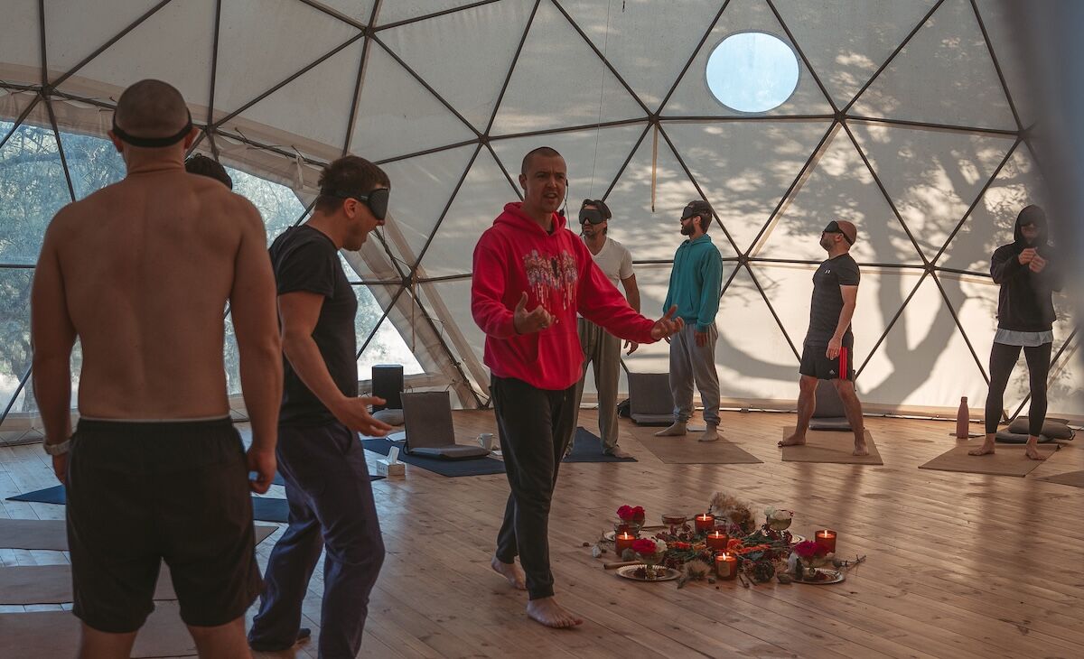 A guide speaks in the dome as blindfolded men stand among candles at The Return of Men retreat, October 2025.