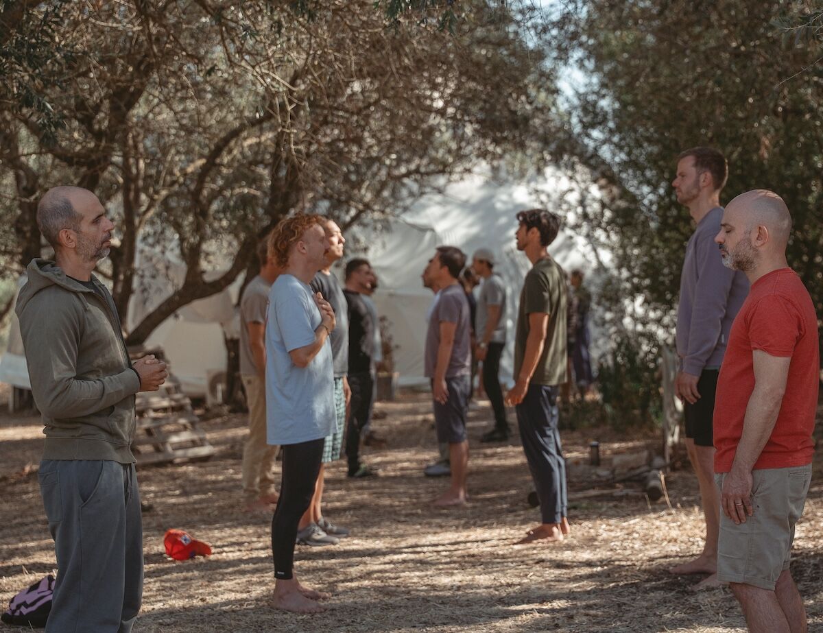 Men stand in two lines facing one another beneath the trees at The Return of Men retreat, Arrábida, 2025.