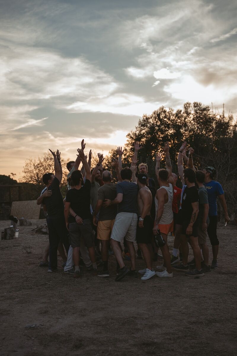 Men raising their hands in celebration during a retreat at sunset, symbolising transformation, clarity, and connection for high-performing leaders.