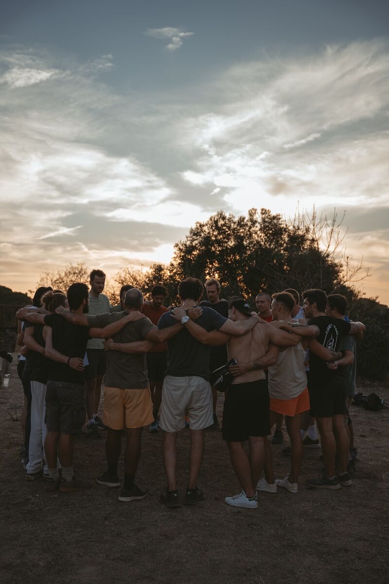 Group of men from the Return of Men Retreat embracing at sunset after ritual combat, symbolising brotherhood, release, and transformation.