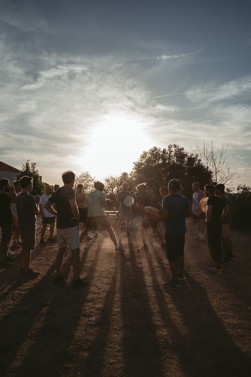 The men gather on a dusty track in low sunlight at The Return of Men retreat, Arrábida, Portugal, October 2025.