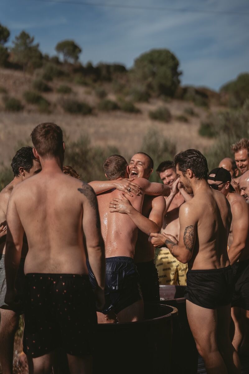 Two men hugging joyfully surrounded by brothers, representing authentic connection and brotherhood.