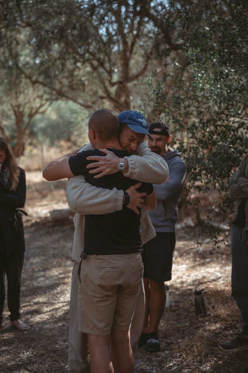 Two men hugging surrounded by others, symbolising support, brotherhood, and the courage to pause and reconnect with the authentic self.