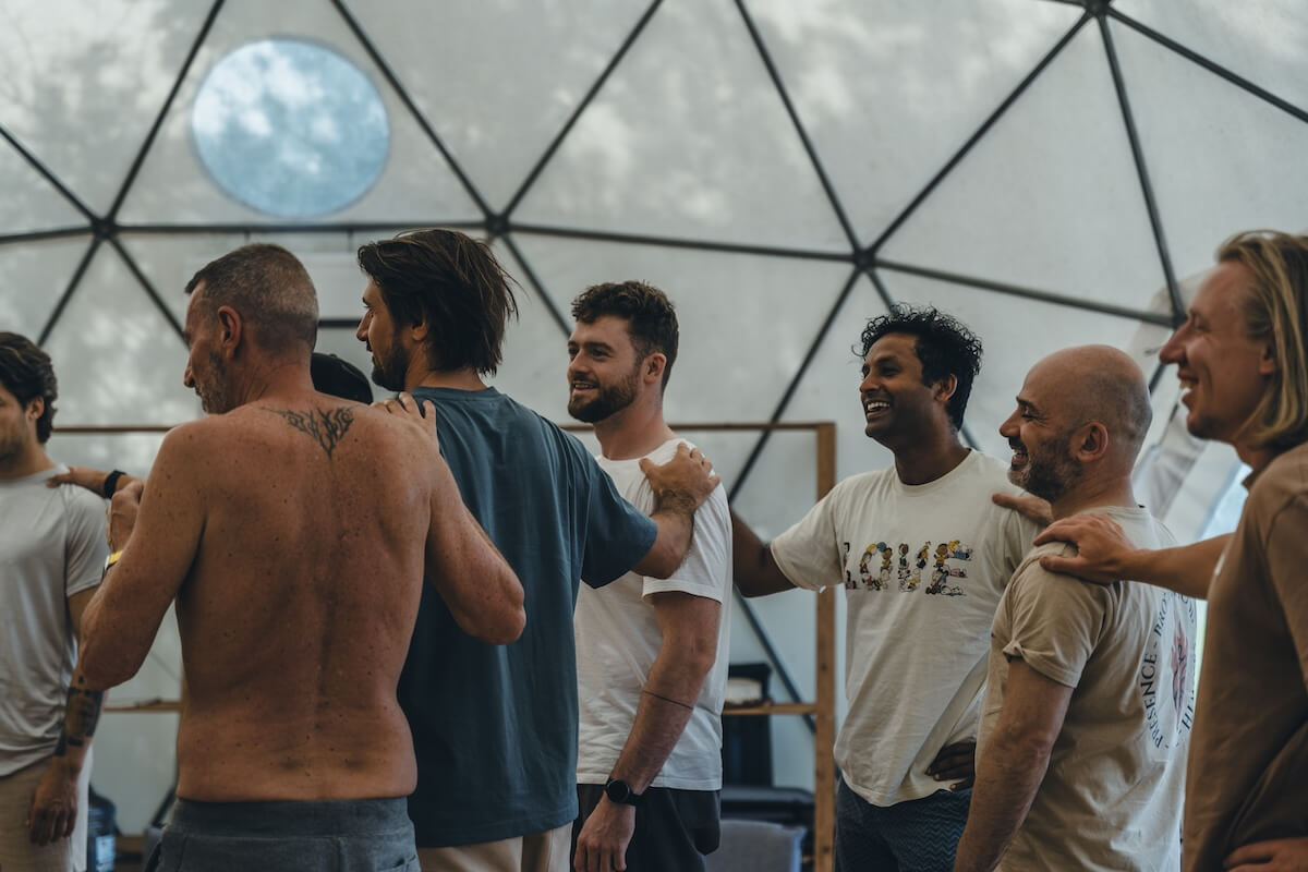 Men stand in a smiling line, hands on each other's shoulders, in the dome at The Return of Men retreat, 2026.
