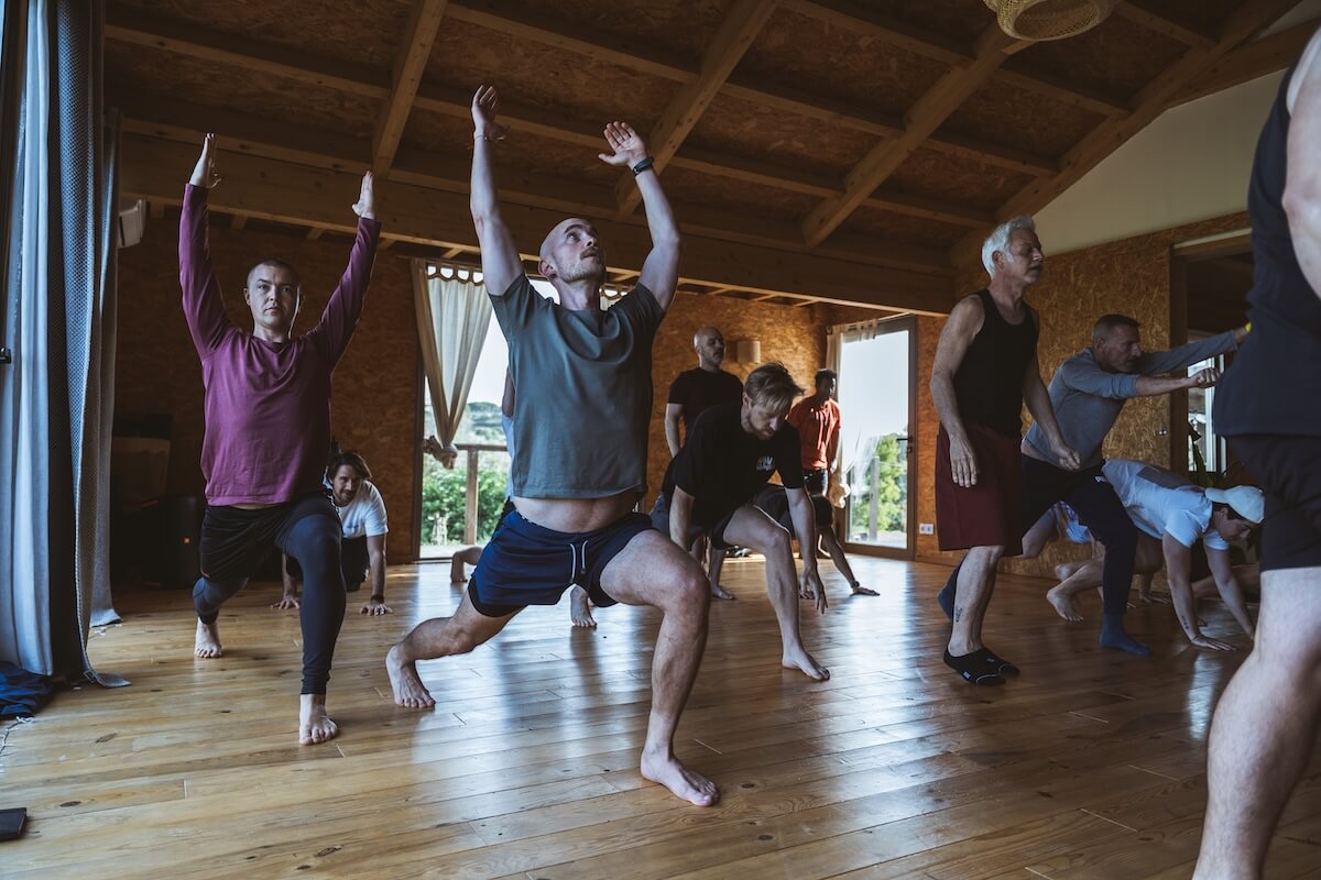 Men move through a standing practice, arms raised, in the wooden hall at The Return of Men retreat, Portugal, 2026.