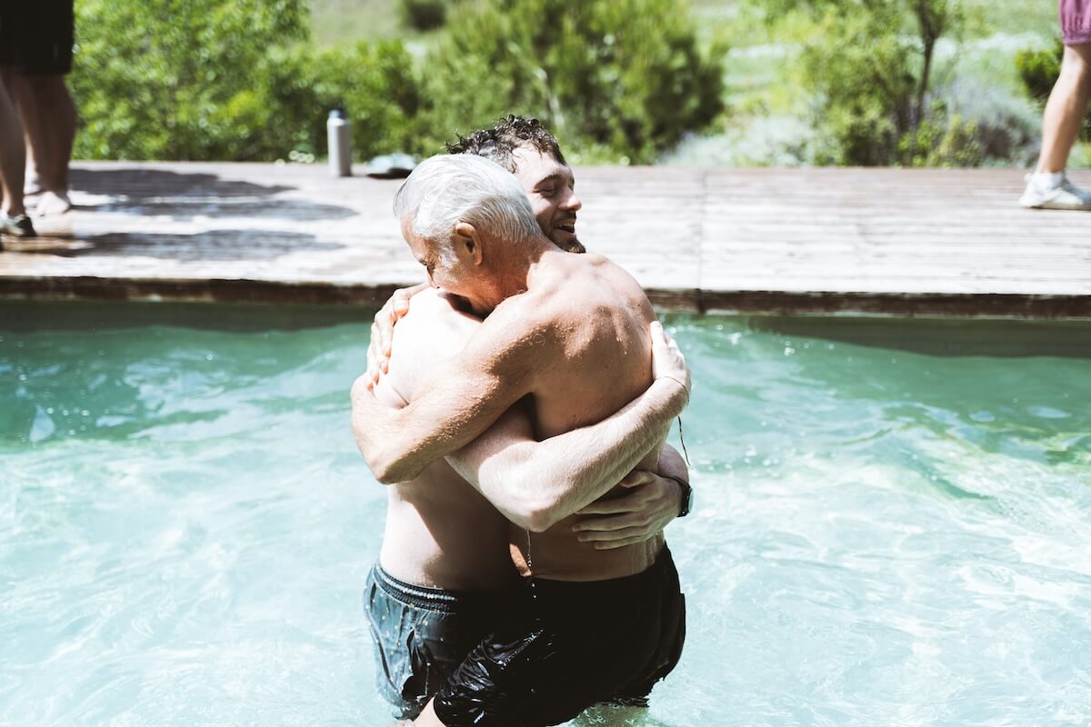 Two men embrace chest-deep in the pool at The Return of Men retreat, BioVilla, May 2026.