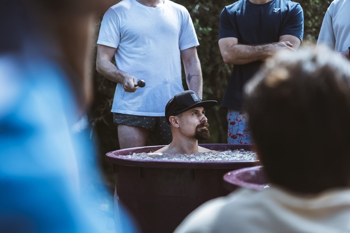 A bearded man in a cap sits in the ice bath, gaze lifted, at The Return of Men retreat, Portugal, May 2026.