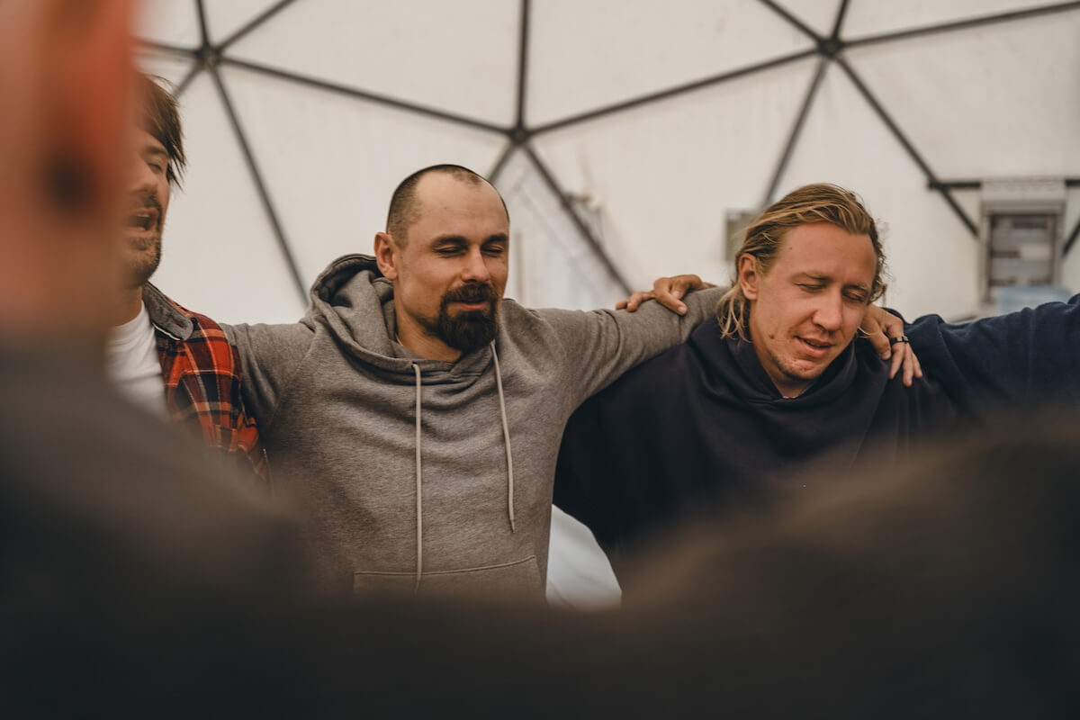 Men stand arm in arm with eyes closed in the closing circle in the dome at The Return of Men retreat, May 2026.