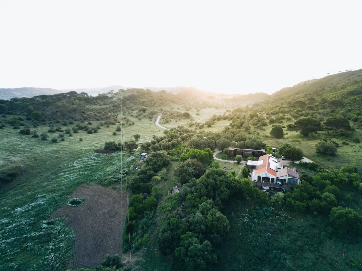 BioVilla from the air at sunset, folded into the green hills of the Arrábida Natural Park, Portugal.