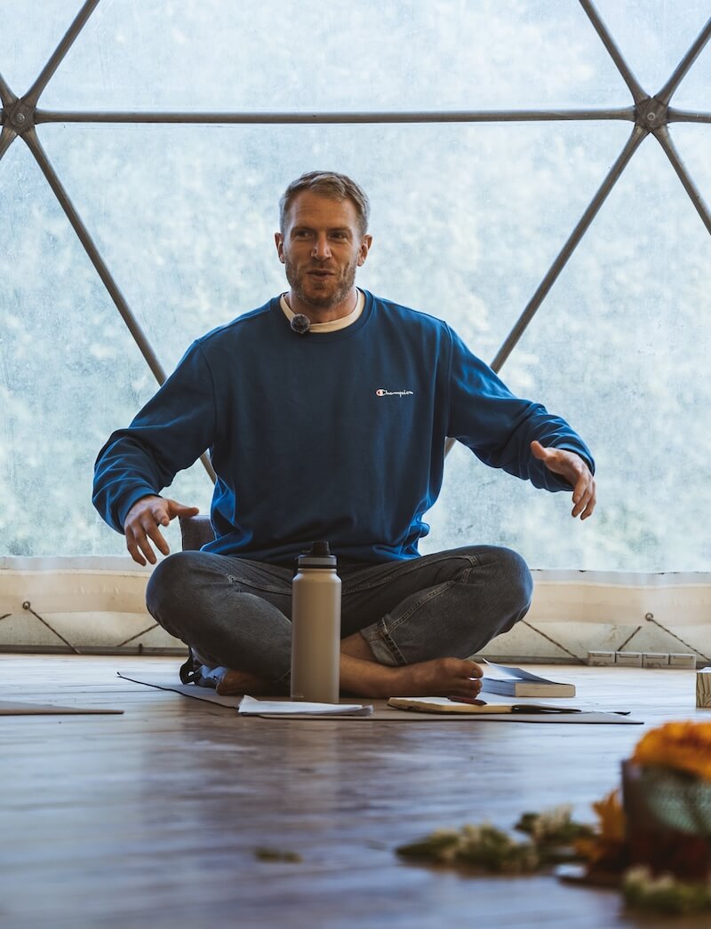 A facilitator speaks cross-legged before the circle in the geodesic dome at The Return of Men retreat, BioVilla, 2026.