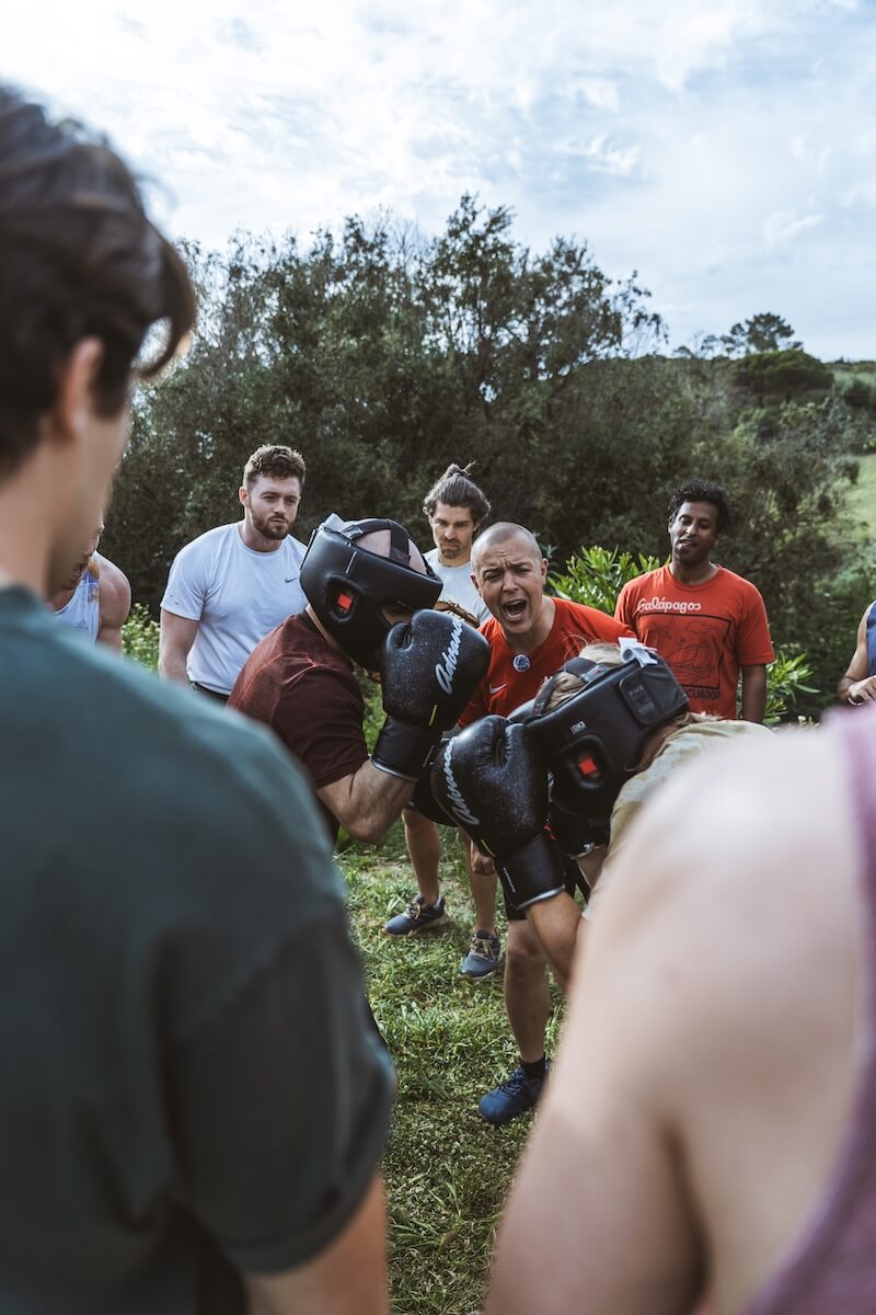 Two men clinch mid-bout as the circle watches on the hillside at The Return of Men retreat, Arrábida, 2026.