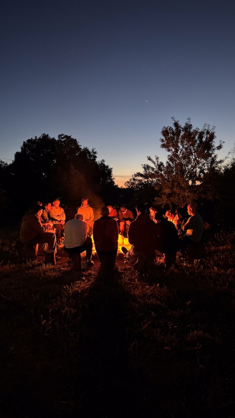Men sitting together around the fire circle at dusk during a 5-day men's retreat in Arrábida, Portugal