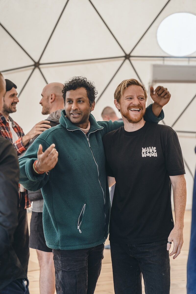 Two men stand arm in arm, mid-laugh, in the geodesic dome at The Return of Men retreat, Portugal, 2026.