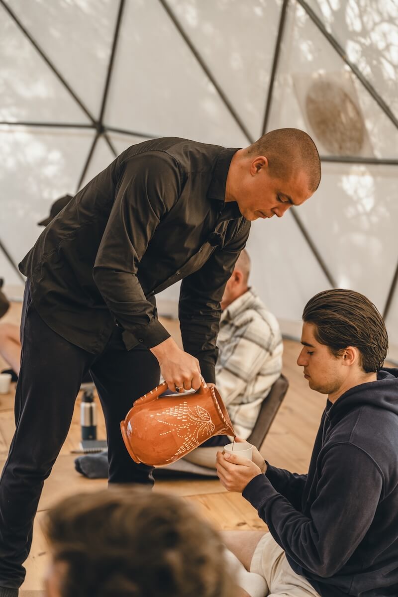 Ceremonial cacao is poured from a clay jug into a man's cup in the dome at The Return of Men retreat, 2026.