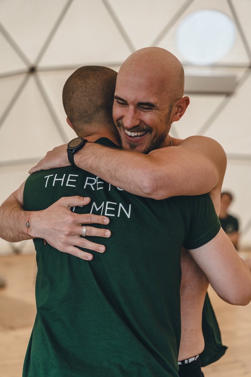 Two men embracing and smiling in the retreat shirts at the close of The Return of Men retreat in Portugal