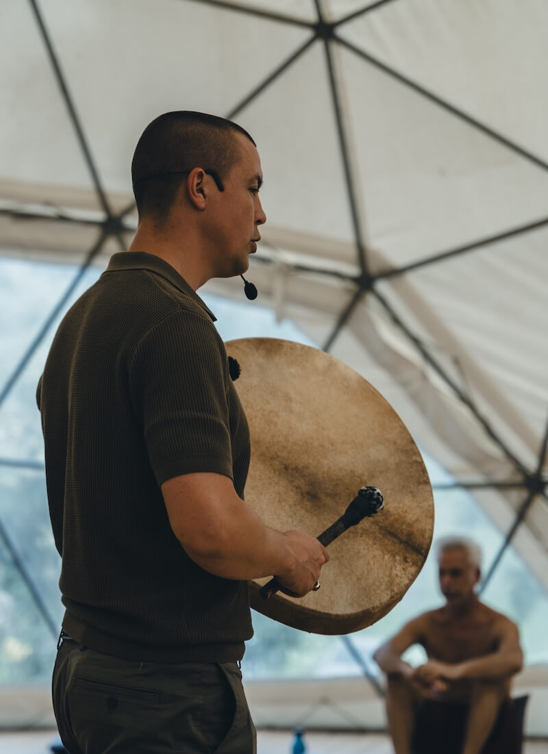 A facilitator leads with a frame drum inside the dome at The Return of Men retreat, BioVilla, Portugal, 2026.