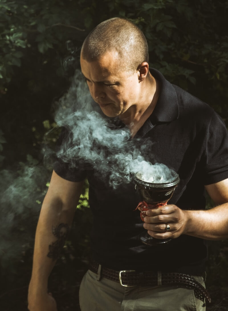 A facilitator carries a smoking copal cup through the trees at The Return of Men retreat, Portugal, 2026.