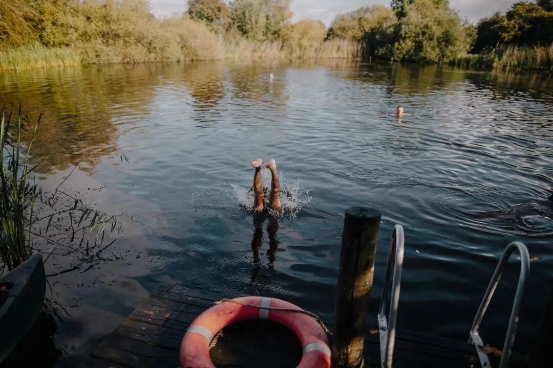 A man dives into the wild swimming pond at Elmore, feet mid-air beside the jetty