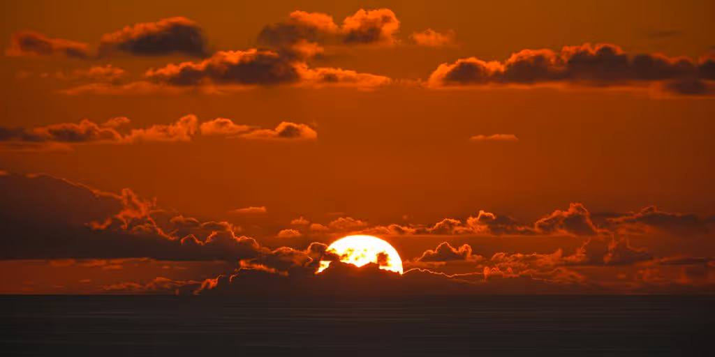 the sun is setting over the ocean with clouds