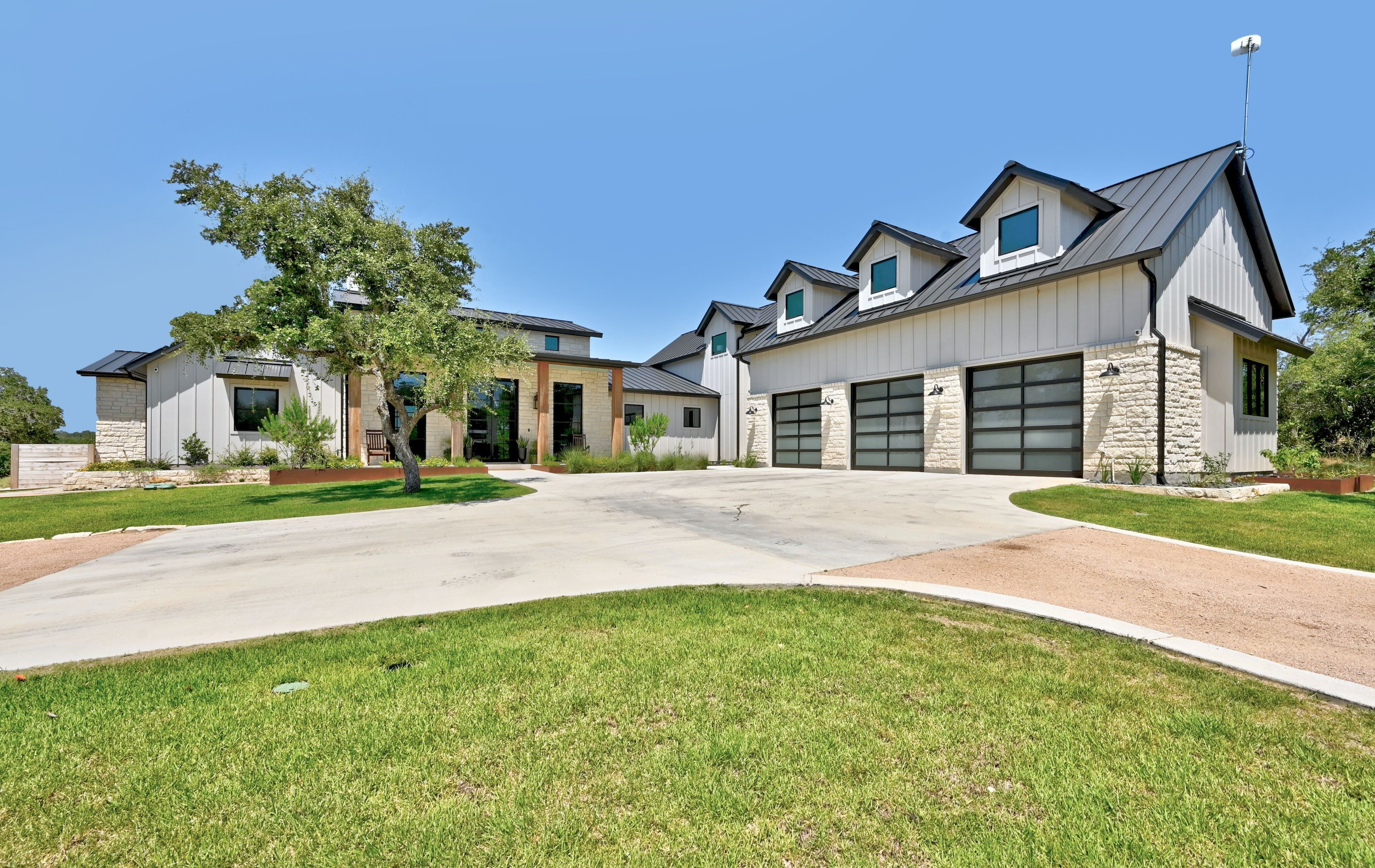 White farmhouse with a dark metal roof, three garage doors and a wide driveway