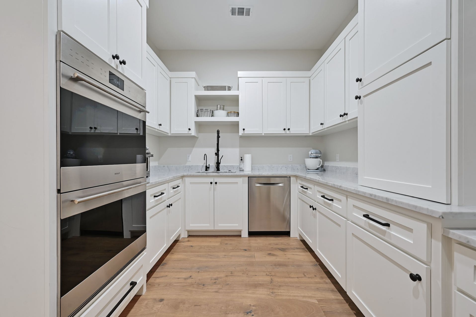 Galley kitchen with white cabinets and double wall ovens