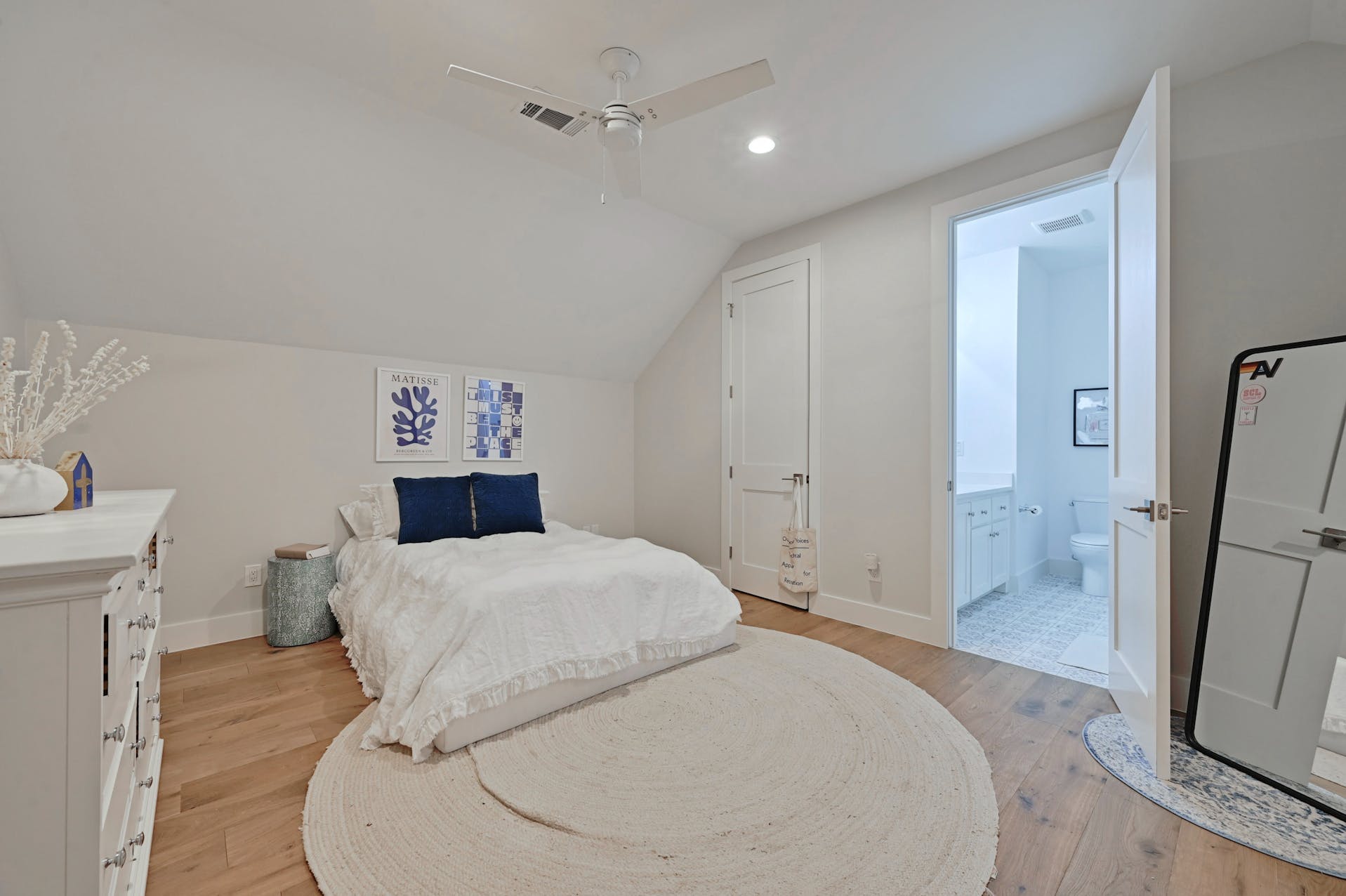 Bedroom with white bedding, a round rug and sloped ceiling