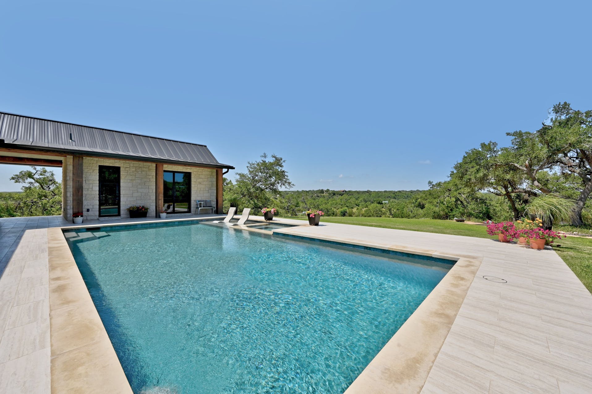 Pool with a stone deck beside a metal-roofed wing of the home