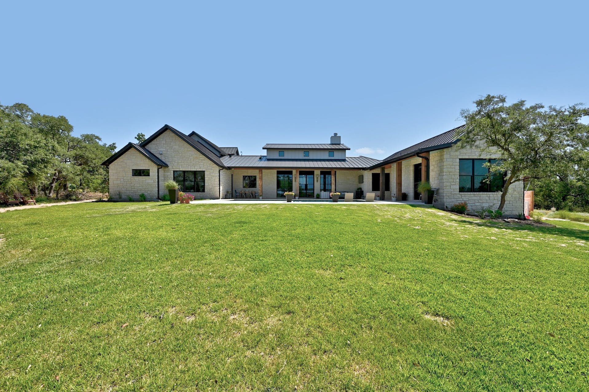 Rear exterior of the home across a wide lawn with oak trees