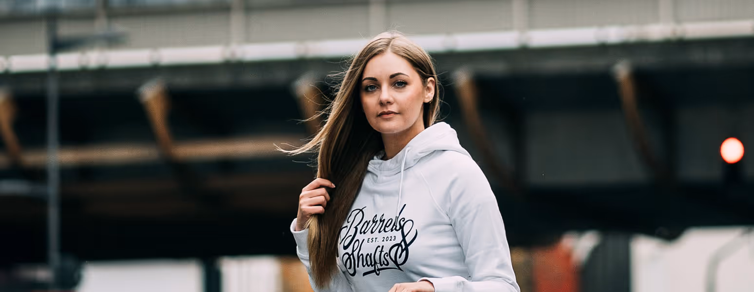 young woman wearing barrels & shafts hoodie infront of a bridge