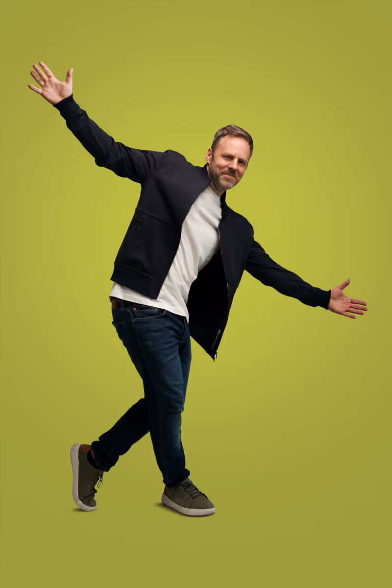 Robert Bittig bei Fotoshooting mit ausgebreiteten Armen und überkreuz Schritt vor einem Hellgrünen Hintergrund.