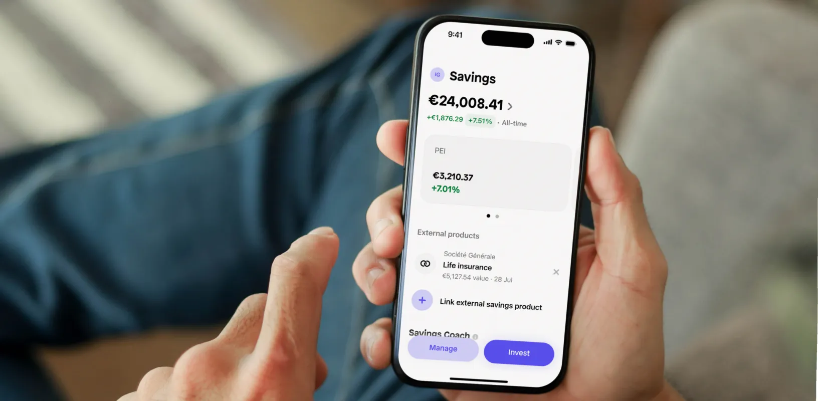 Hand holding smartphone displaying a financial app showing savings account balance of €24,008.41 with 7.51% all-time growth, PEI Soles balance of €3,210.37 with 7.01% growth, external product life insurance valued at €5,127.54, and buttons labeled Manage and Invest.