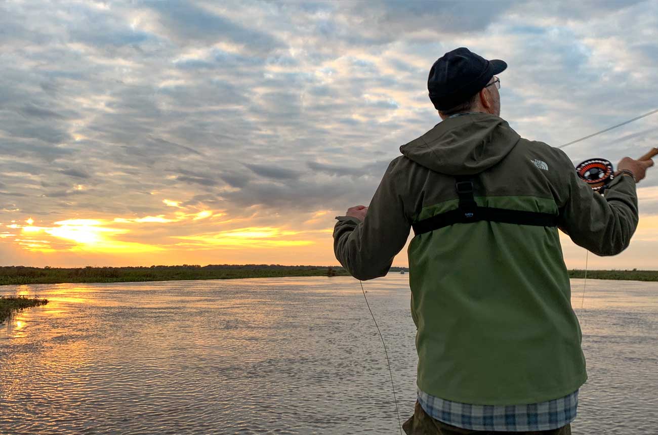 Angler in a rain jacket and cap casting at sunset on the Paraná