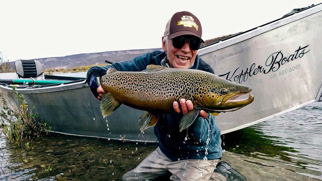 Angler with a brown trout catch by the drift boat at Bravo Sur Lodge