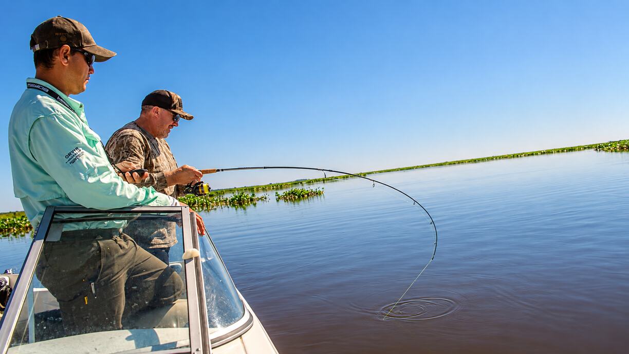 Angler fighting a fish on a bent spinning rod as the guide watches
