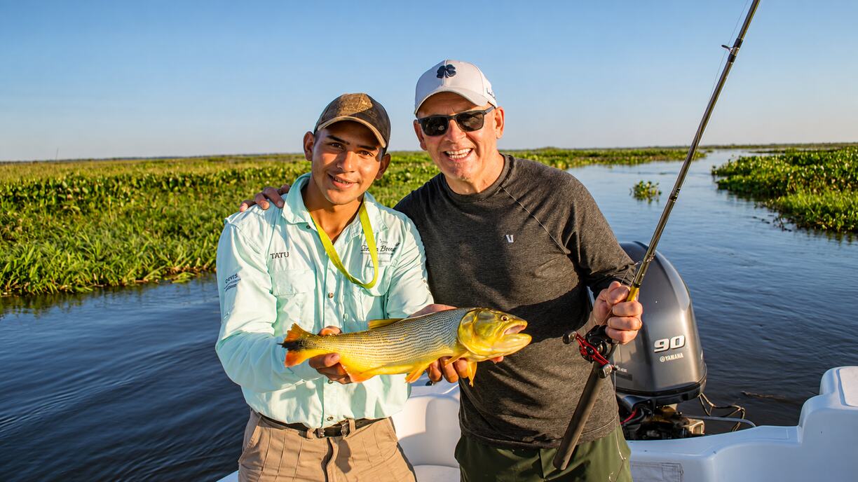 Guide and angler with a golden dorado, baitcasting rod in hand