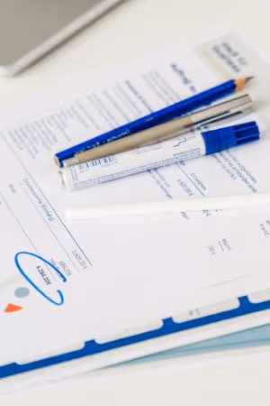 Blauer Stift, Marker und Bleistift liegen auf einem Stapel von Dokumenten mit Grafiken und Zahlen.